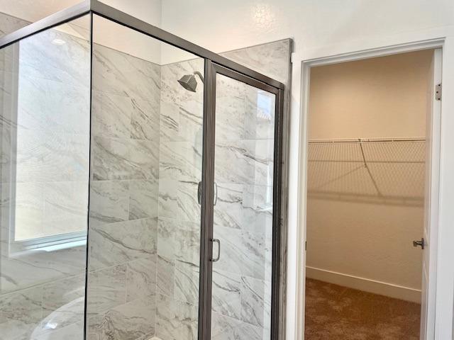 full bathroom featuring a shower stall, baseboards, and a walk in closet