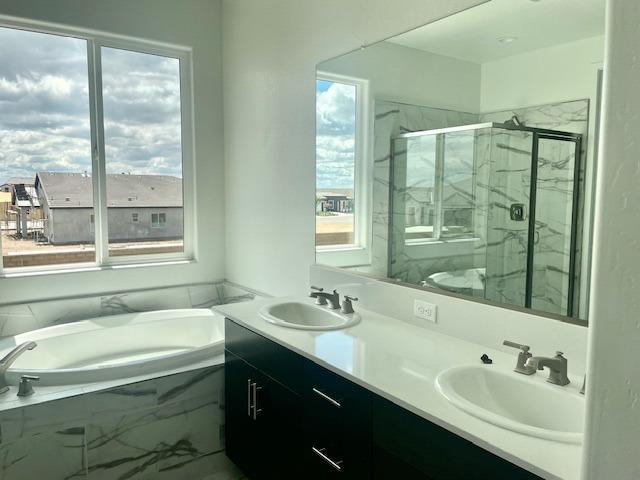 bathroom with double vanity, a marble finish shower, a sink, and a bath