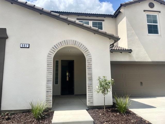 doorway to property featuring a tiled roof, an attached garage, driveway, and stucco siding