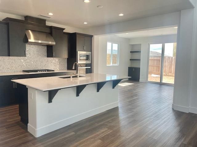 kitchen with wall chimney exhaust hood, appliances with stainless steel finishes, a breakfast bar area, and a center island with sink