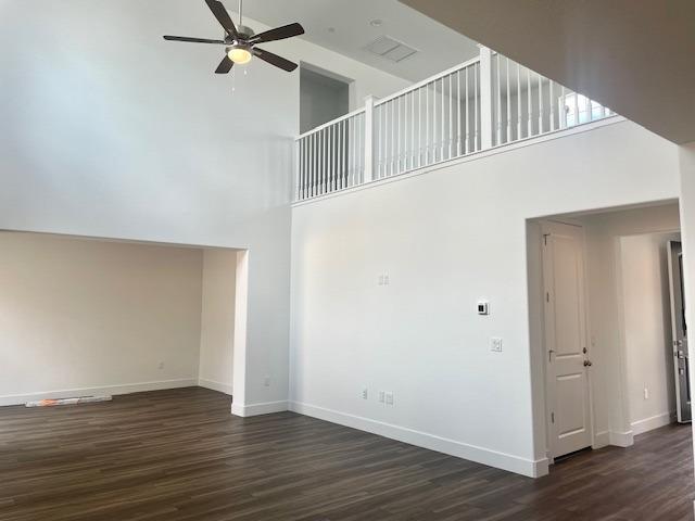 unfurnished living room featuring visible vents, a towering ceiling, wood finished floors, baseboards, and ceiling fan