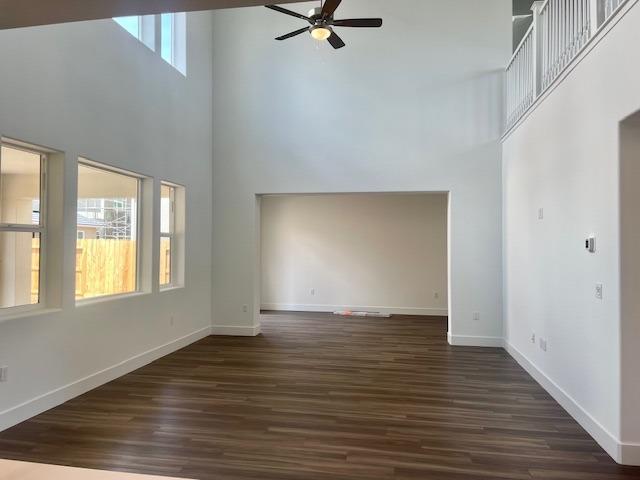 unfurnished living room featuring baseboards, a towering ceiling, ceiling fan, and dark wood-style flooring