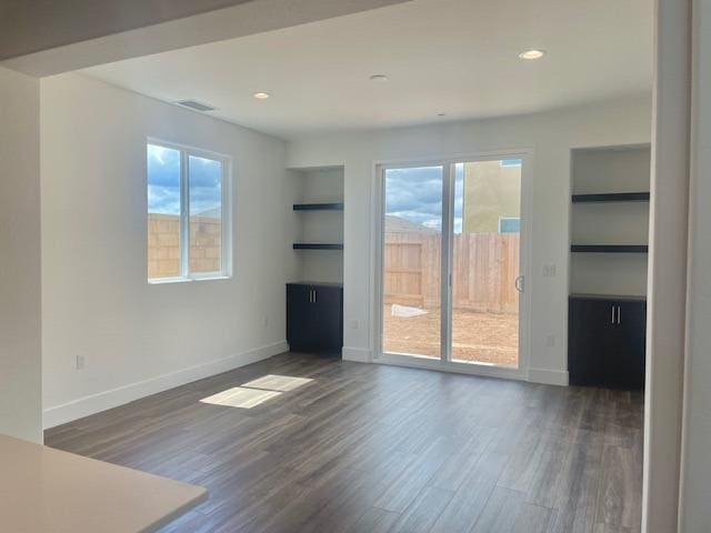 unfurnished living room with dark wood-style flooring, visible vents, built in shelves, baseboards, and recessed lighting