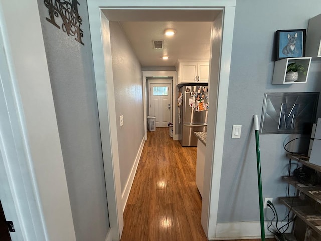 hall featuring visible vents, baseboards, and wood finished floors