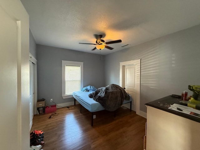 bedroom featuring a textured ceiling, dark wood-type flooring, visible vents, baseboards, and a ceiling fan