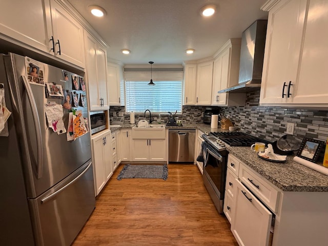 kitchen featuring wall chimney range hood, white cabinetry, appliances with stainless steel finishes, and a sink