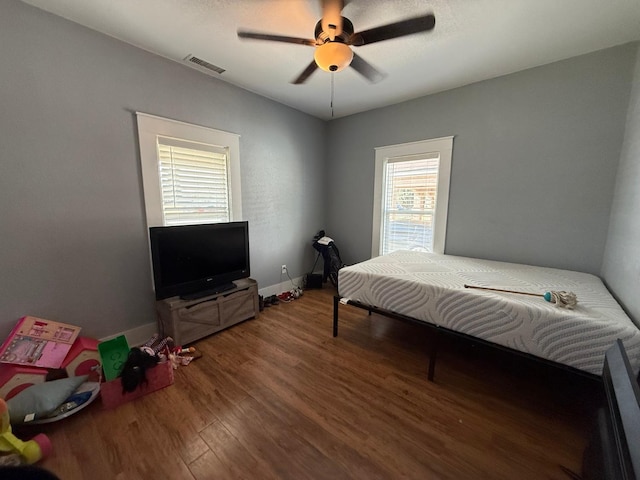 bedroom with ceiling fan, wood finished floors, visible vents, and baseboards