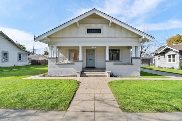 bungalow-style house featuring brick siding, covered porch, a front yard, and fence