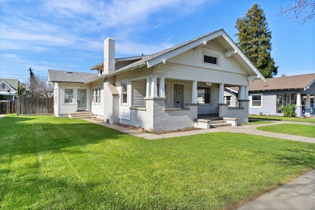 bungalow-style house with brick siding, a front lawn, fence, covered porch, and a chimney