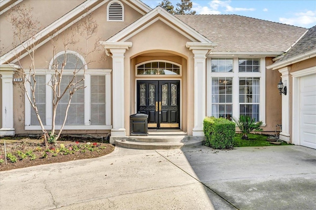 view of exterior entry with a garage, concrete driveway, roof with shingles, french doors, and stucco siding