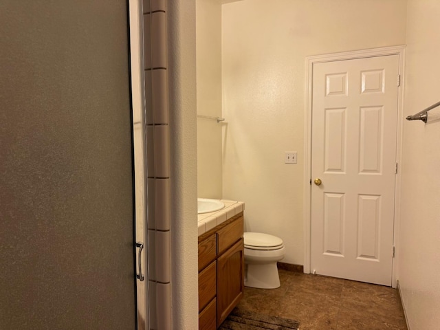 bathroom with toilet, a shower with shower door, vanity, and baseboards