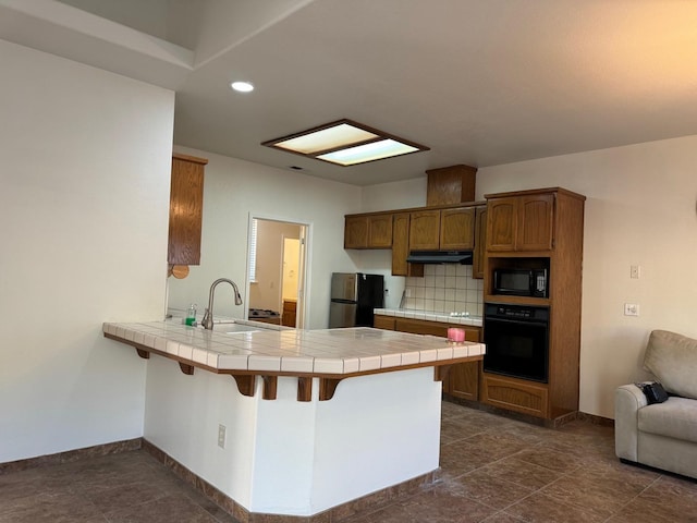 kitchen with tile countertops, brown cabinets, a peninsula, black appliances, and a sink