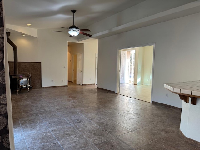 unfurnished living room featuring ceiling fan, a wood stove, and baseboards