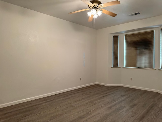 spare room featuring dark wood-style flooring, visible vents, and baseboards