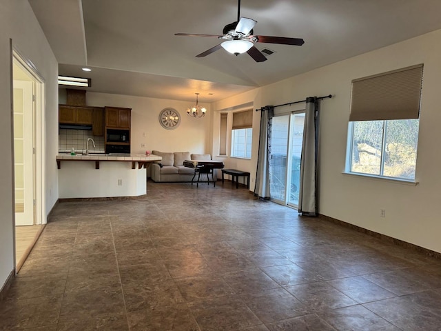 unfurnished living room featuring lofted ceiling, baseboards, a sink, and ceiling fan with notable chandelier