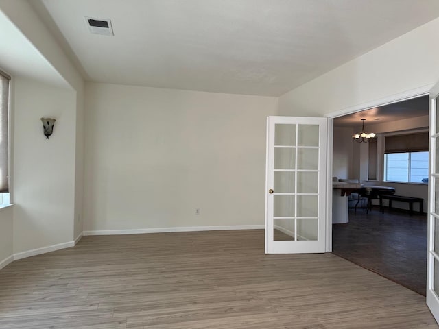 unfurnished room with a chandelier, visible vents, baseboards, and wood finished floors