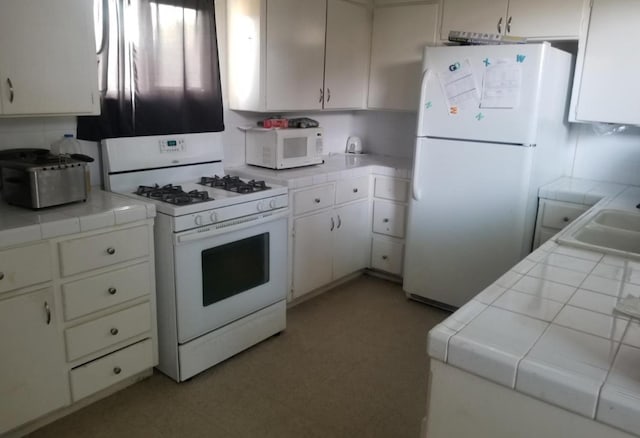 kitchen with tile countertops, light floors, white cabinetry, a sink, and white appliances