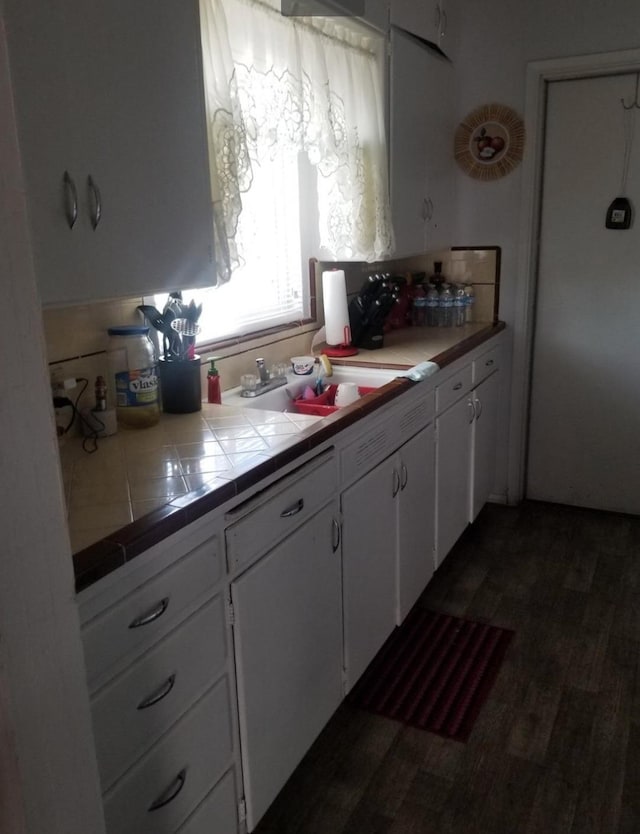 kitchen with tile countertops, dark wood-style flooring, white cabinets, and a sink