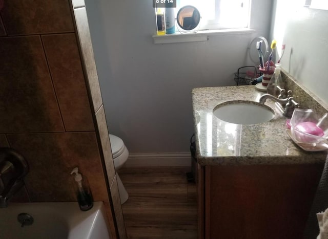 bathroom featuring a bathing tub, toilet, wood finished floors, vanity, and baseboards