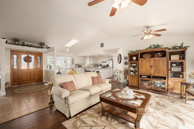 living area featuring light wood finished floors, vaulted ceiling with skylight, and ceiling fan