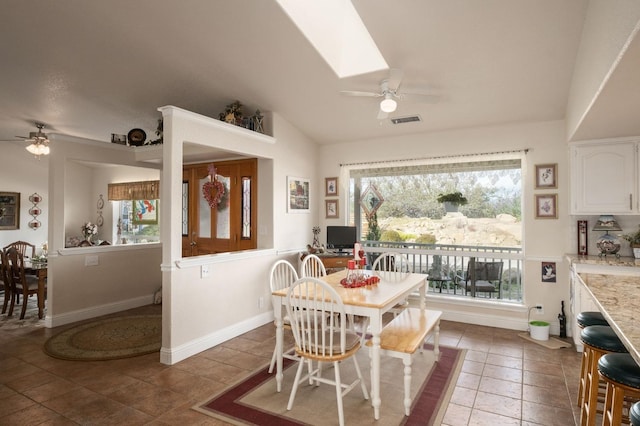 tiled dining room with visible vents, vaulted ceiling with skylight, a ceiling fan, and baseboards