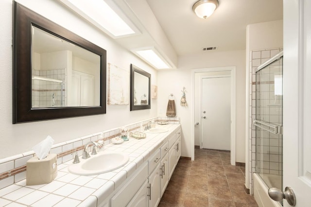 full bath with double vanity, a shower with shower door, visible vents, and a sink