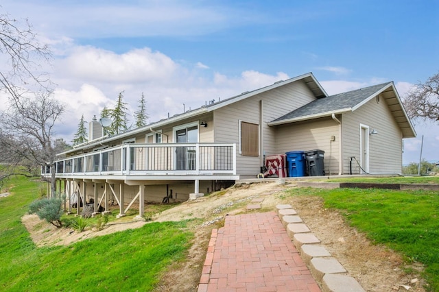 rear view of house with a chimney, a wooden deck, and a yard