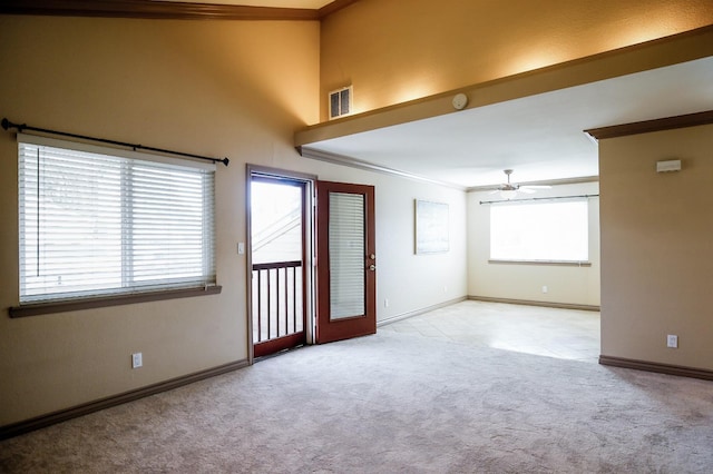 empty room with a healthy amount of sunlight, a ceiling fan, crown molding, and light colored carpet