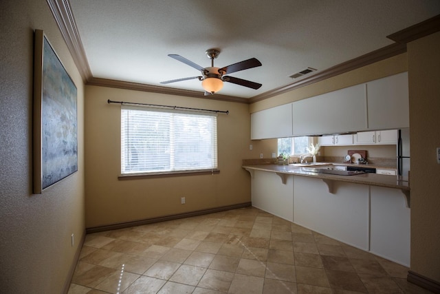 kitchen featuring visible vents, ornamental molding, a peninsula, white cabinetry, and a sink