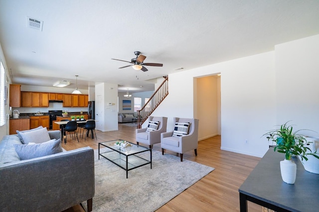 living room with stairs, light wood finished floors, visible vents, and baseboards