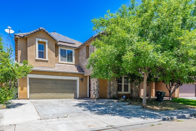 traditional-style home with a garage, stone siding, driveway, roof mounted solar panels, and stucco siding