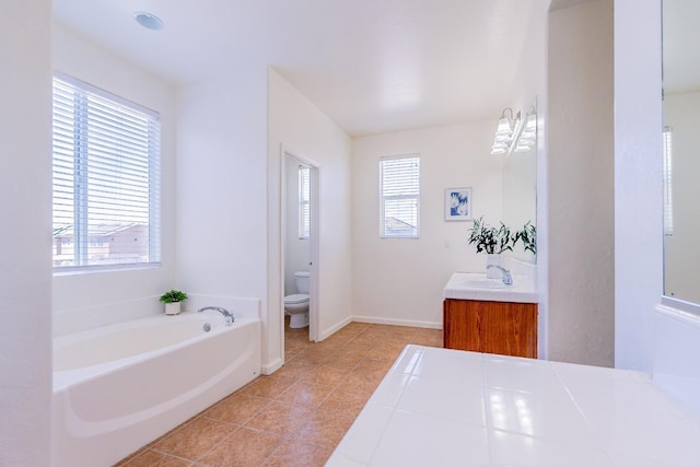 bathroom with a garden tub, tile patterned flooring, toilet, vanity, and baseboards