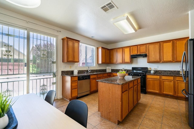 kitchen with under cabinet range hood, a kitchen island, visible vents, black appliances, and brown cabinetry