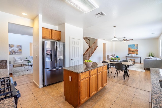 kitchen featuring light tile patterned floors, visible vents, a kitchen island, dark stone countertops, and stainless steel fridge with ice dispenser