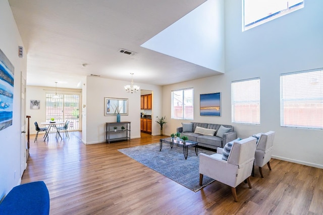 living room featuring light wood finished floors, visible vents, a chandelier, and baseboards