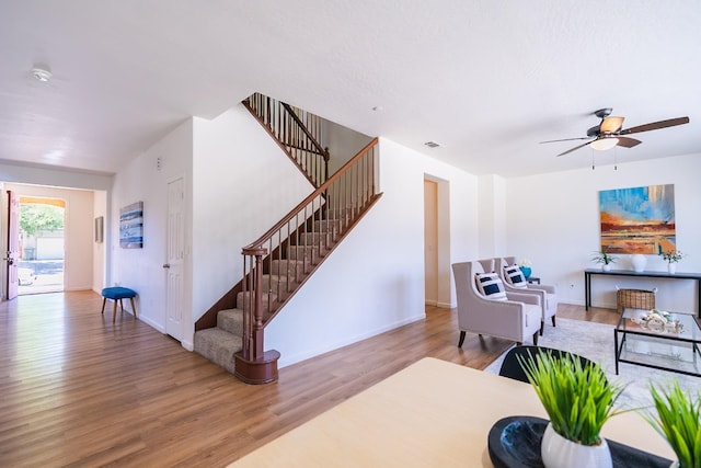 living room featuring baseboards, visible vents, ceiling fan, stairway, and wood finished floors