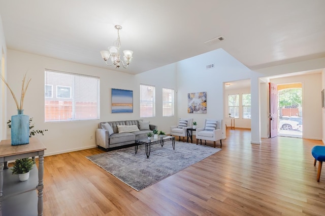 living area featuring a chandelier, light wood-type flooring, lofted ceiling, and visible vents