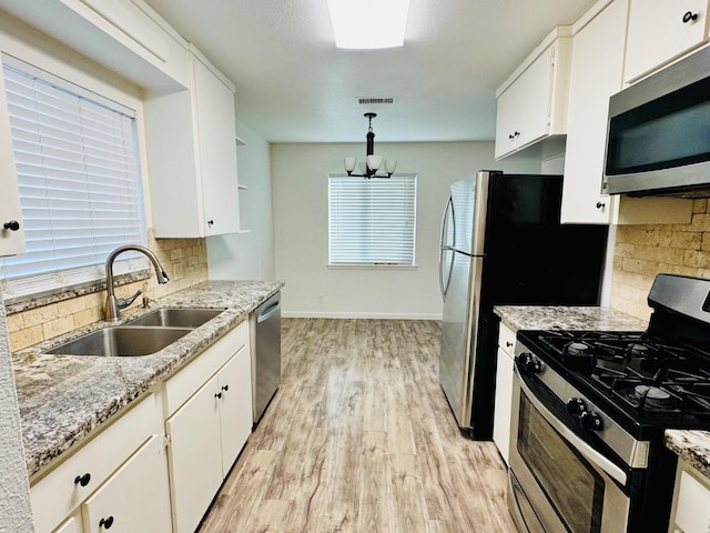 kitchen featuring decorative light fixtures, light wood finished floors, appliances with stainless steel finishes, white cabinets, and a sink