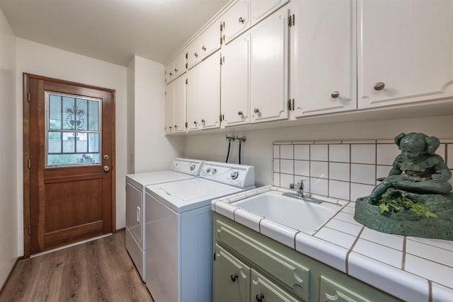 clothes washing area with cabinet space, a sink, washing machine and clothes dryer, and wood finished floors