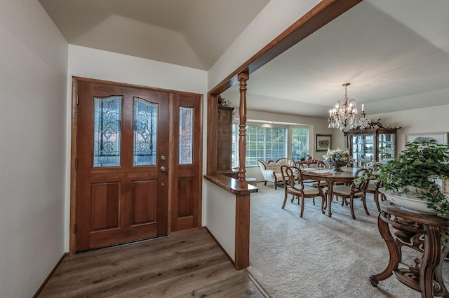 carpeted foyer featuring a notable chandelier, decorative columns, vaulted ceiling, wood finished floors, and baseboards