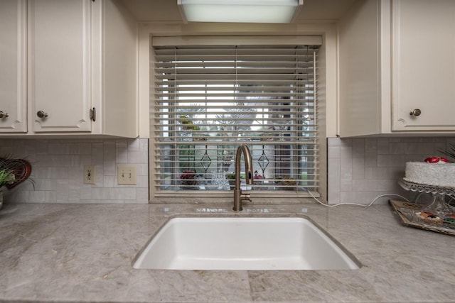 kitchen featuring tasteful backsplash, a sink, light stone counters, and white cabinets