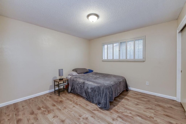 bedroom featuring a textured ceiling, baseboards, and wood finished floors