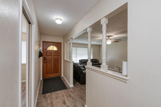 foyer with baseboards, a ceiling fan, a textured ceiling, light wood-type flooring, and ornate columns