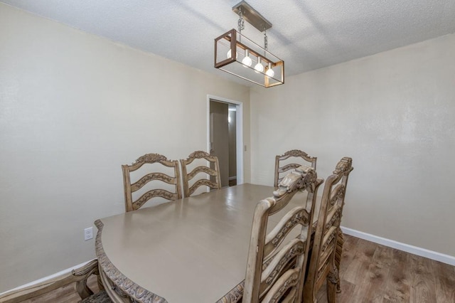 dining area with a textured ceiling, baseboards, and wood finished floors