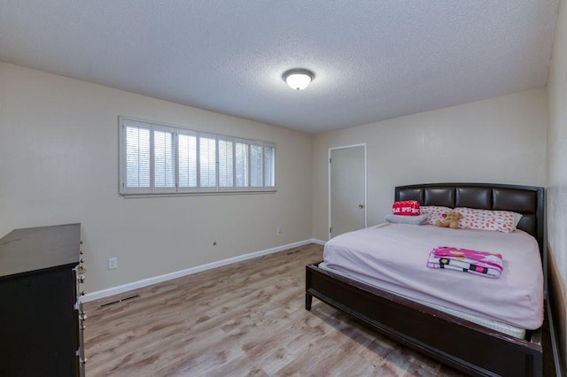 bedroom with a textured ceiling, baseboards, visible vents, and light wood-style floors