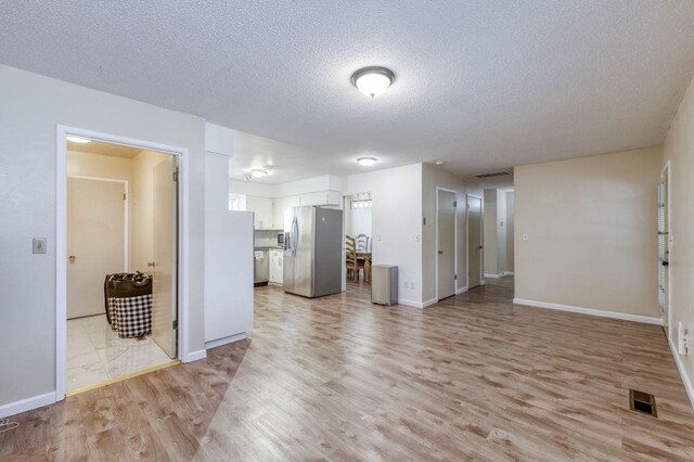 unfurnished living room with baseboards, visible vents, light wood-style flooring, and a textured ceiling