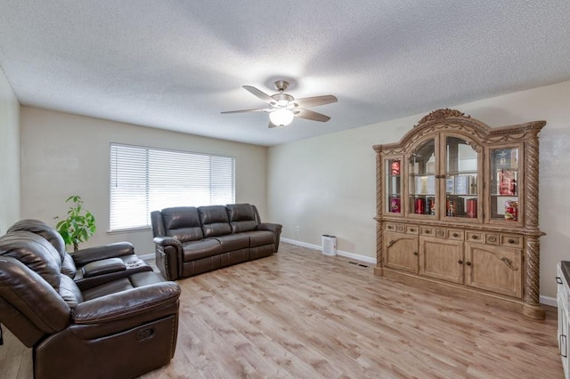 living room featuring baseboards, a textured ceiling, light wood-style flooring, and a ceiling fan