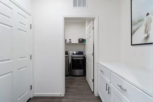 corridor with dark wood-style flooring, washer and clothes dryer, and visible vents