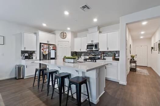 kitchen with appliances with stainless steel finishes, light countertops, white cabinets, and an island with sink