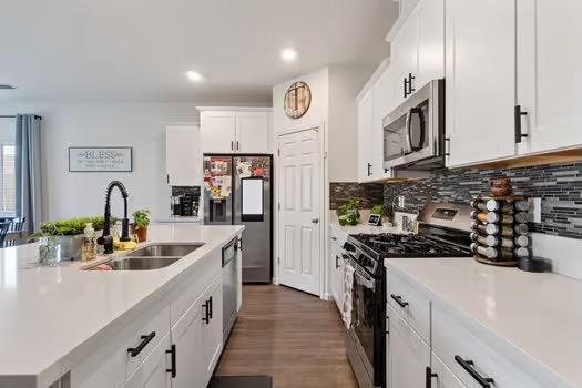 kitchen with stainless steel appliances, light countertops, backsplash, white cabinetry, and a sink